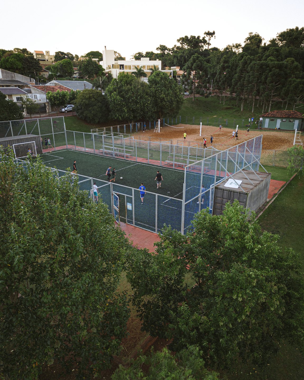 Adulti giocano a calcio e pallavolo in un complesso sportivo all'aperto.