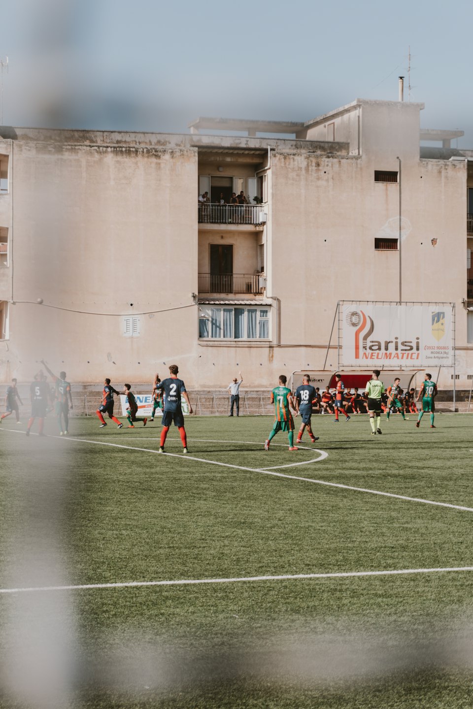 Giocatori di calcio competono su un campo in erba sintetica vicino a un condominio.