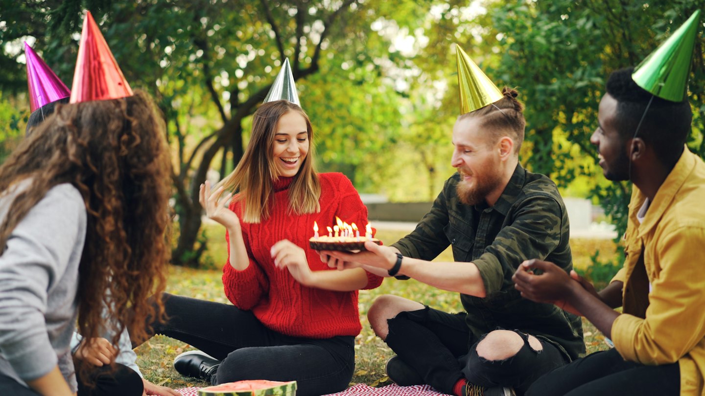 Amici festeggiano un compleanno con torta su una coperta da picnic.